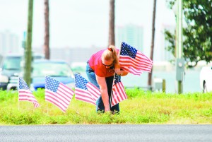 Kim Dekorver places flags in the median near the foot of the Navarre Beach Bridge before the motorcade drove by.  (Photo by Mat Pellegrino | SSRN) 