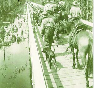 William Milton Broxson (walking) and other family members are depicted leading their cattle herd north over the old Yellow River Bridge. 