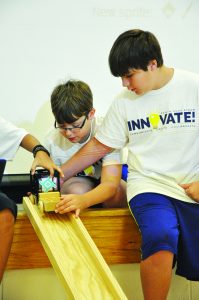 Students from one of the many groups at the Navarre High School STEAM Camp location get ready to test their crash pad using the wooden “Pinewood Derby” car inside the school’s cafeteria. (Photo by Mat Pellegrino | South Santa Rosa News)